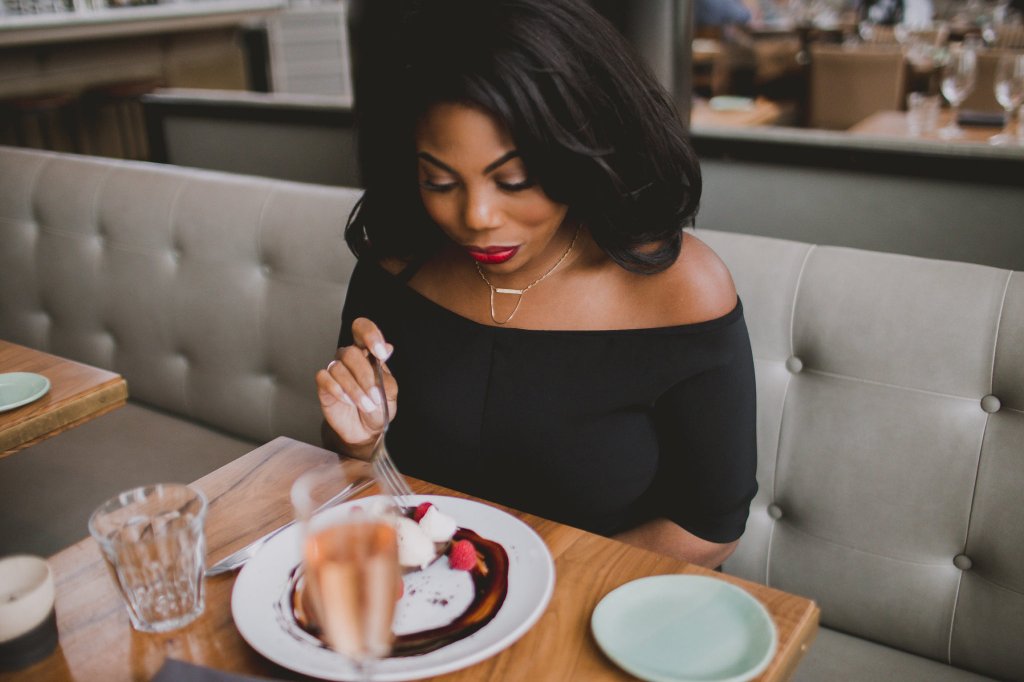 Morgan Kelley wearing red lipstick, sampling dessert at St Cecilia Atlanta with champagne flute in foreground