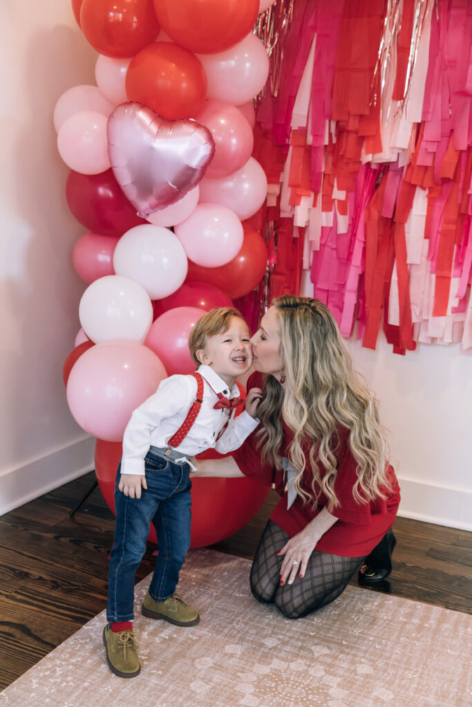 mom kissing preschool son, Valentine's Day balloon installation